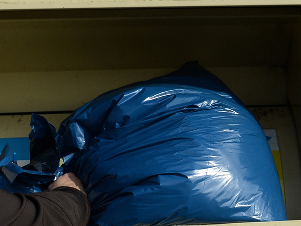 Ein blauer Plastiksack wird in einen Altkleidercontainer geworfen