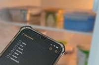 Handy mit einkaufsliste vor dem leeren Kühlschrank